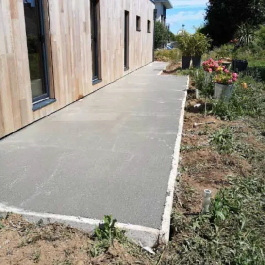 Allée en béton coulée le long d'une maison à bardage bois